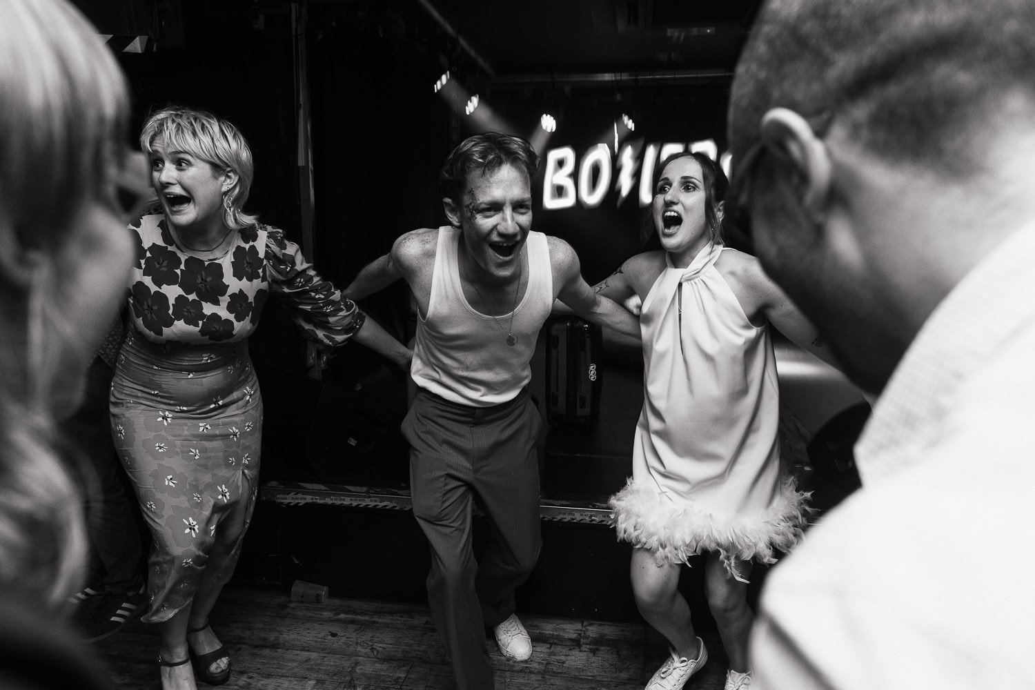 Wedding reception, dancing to Hokey Cokey by Black Lace at the Boileroom. Arms around each other and running in towards the middle. Blonde person in a Never Fully Dressed Davina Mix Print Floral Leopard Animal Midi Dress.