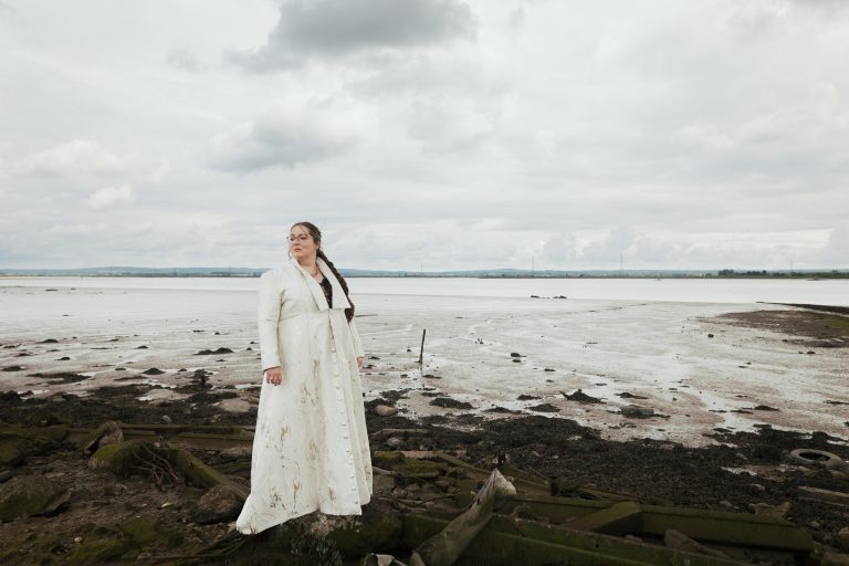 The Ferry House Waterside Wedding Venue in Kent: Bride wearing a Silk Jacquard Brocade Fabric in champagne. A bespoke slow fashion design by Jatin Patel, Kalikas Armour. Under grey skies.