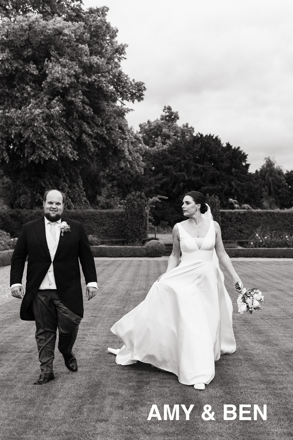 Newly married couple walking along the lawn on a windy wedding day in Newmarket for a Jockey Club Rooms wedding. Amy & Ben text.