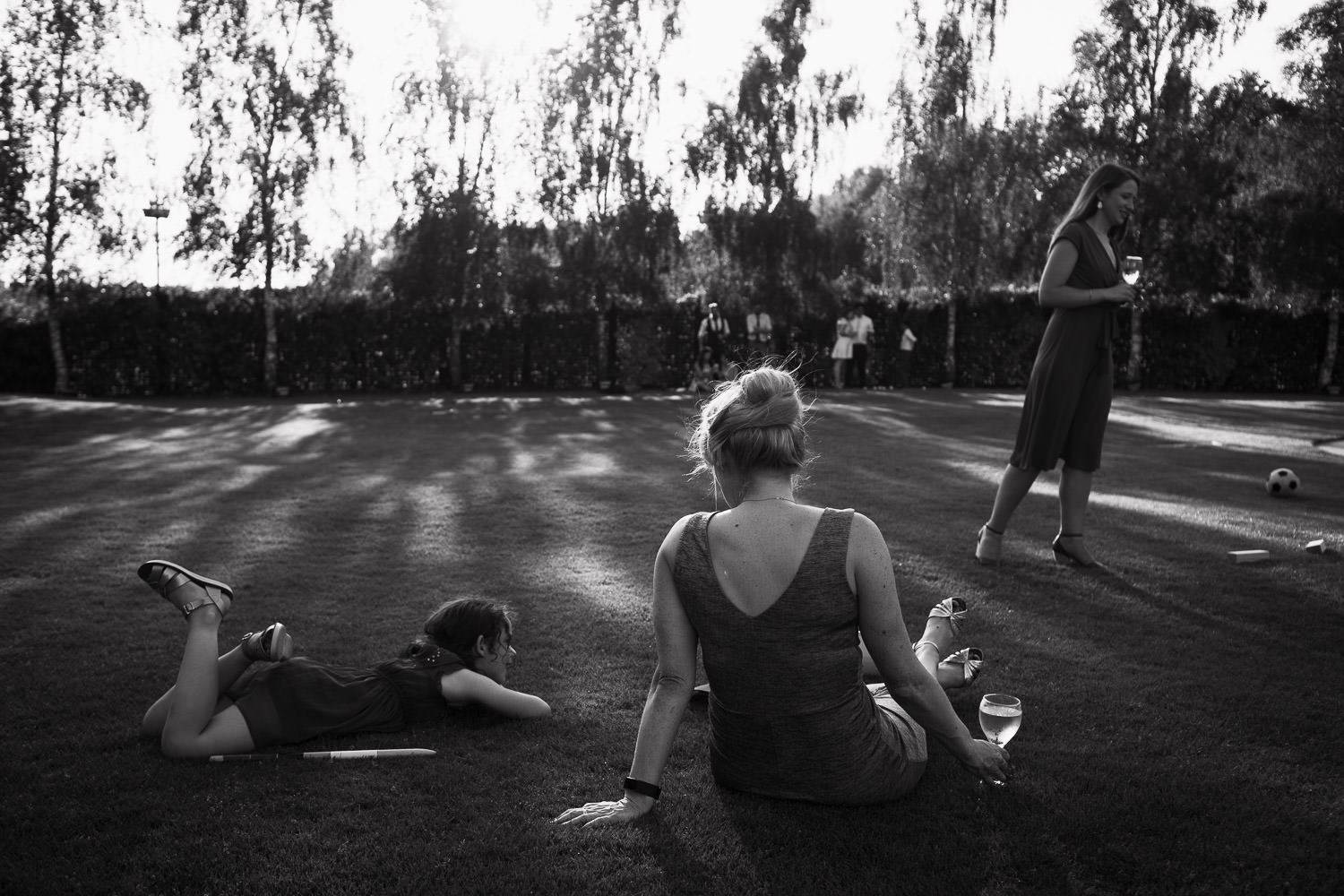 Crondon Park Wedding: Candid photography of wedding guests sat on the lawn in the summer evening light.