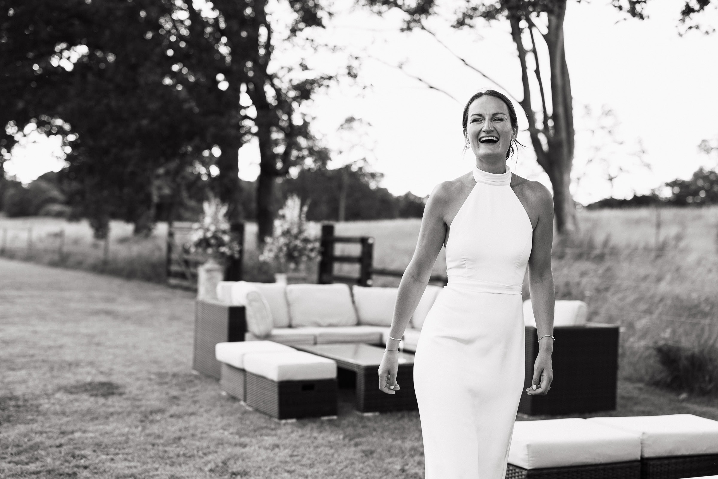 Natural, candid portrait of a joyful bride in a white halterneck dress by Katrine Mogensen. Captured in a Norfolk meadow, this unposed, documentary-style wedding photo showcases the beauty of authentic moments.