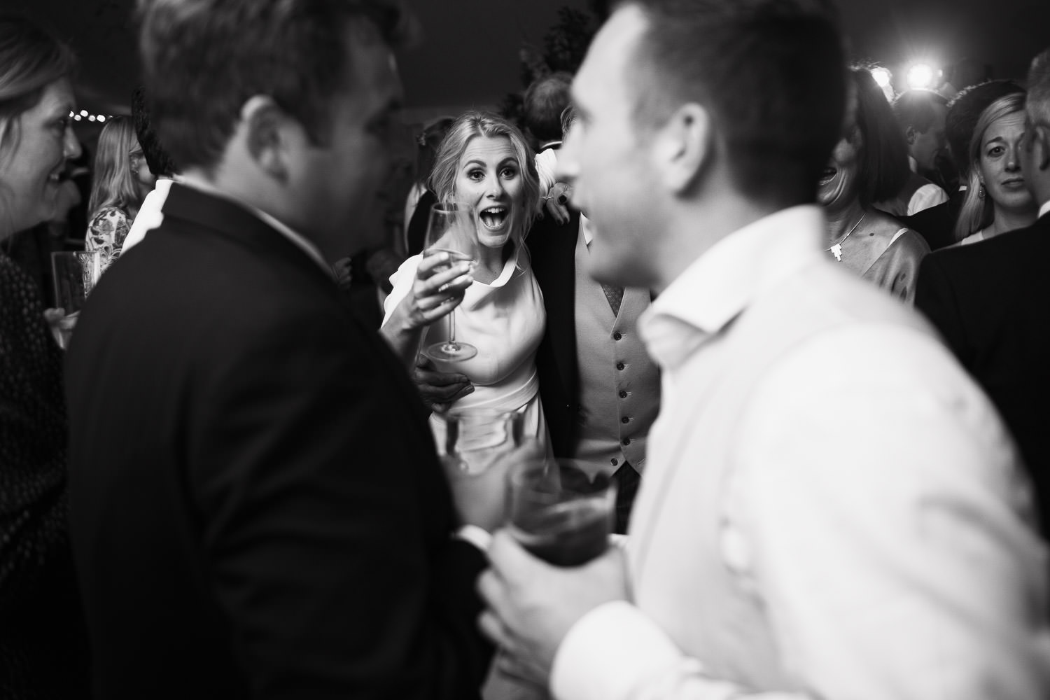 Bride holding a glass of wine, surrounded by guests on the dance floor in a Sail & Peg marquee at a vineyard near South Woodham Ferrers. Essex wedding photography, wearing a Miss Bush Bridal dress