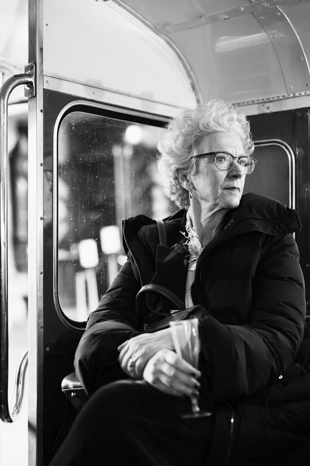 Candid wedding portrait of mother of the bride in London on a bus. She's holding an empty plastic champagne flute. Outside Hackney Town Hall.