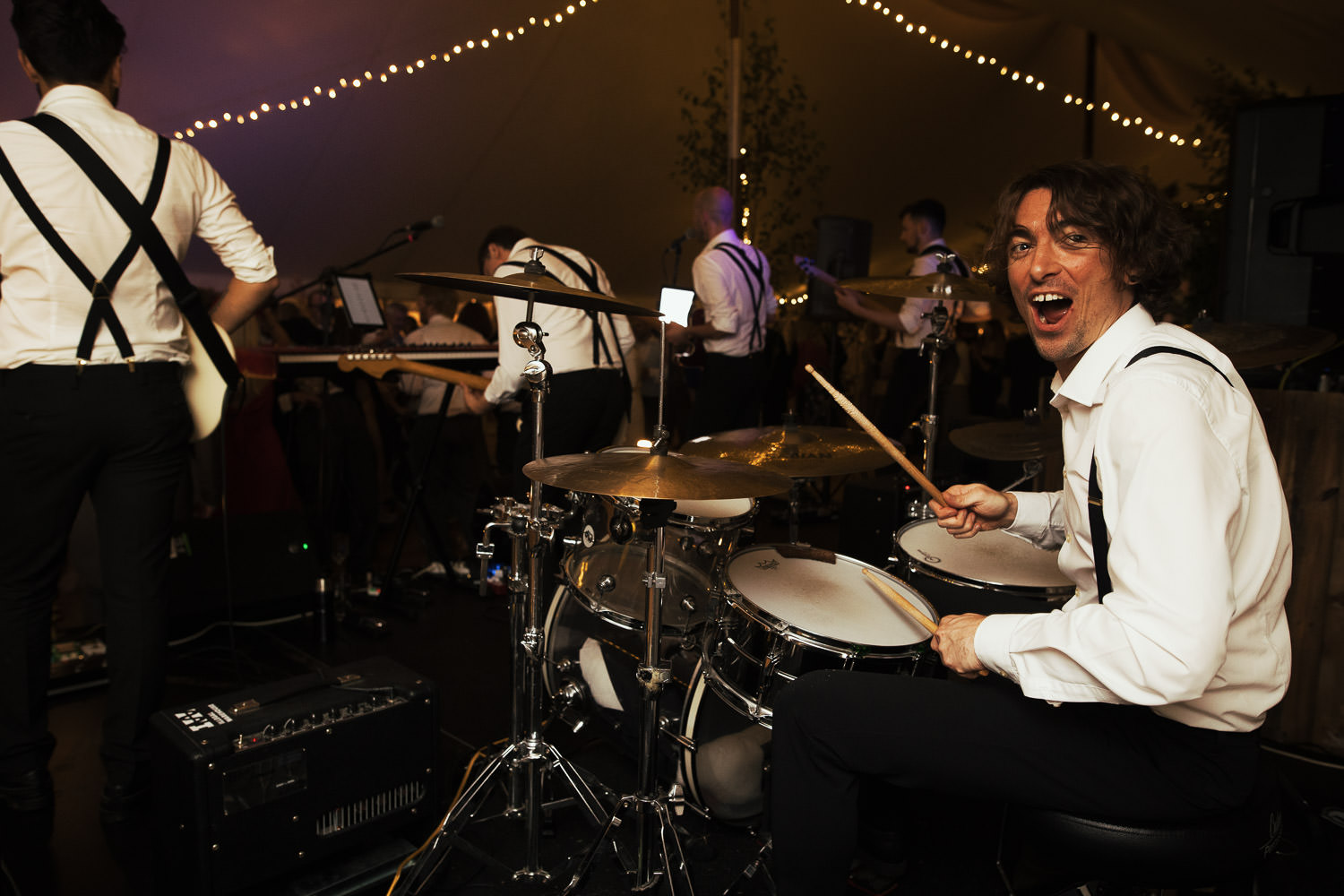 Will Daly on drums in Winston and the Lads looking at the camera at a wedding near South Woodham Ferrers. A reception held in a marquee from Sail and Peg.