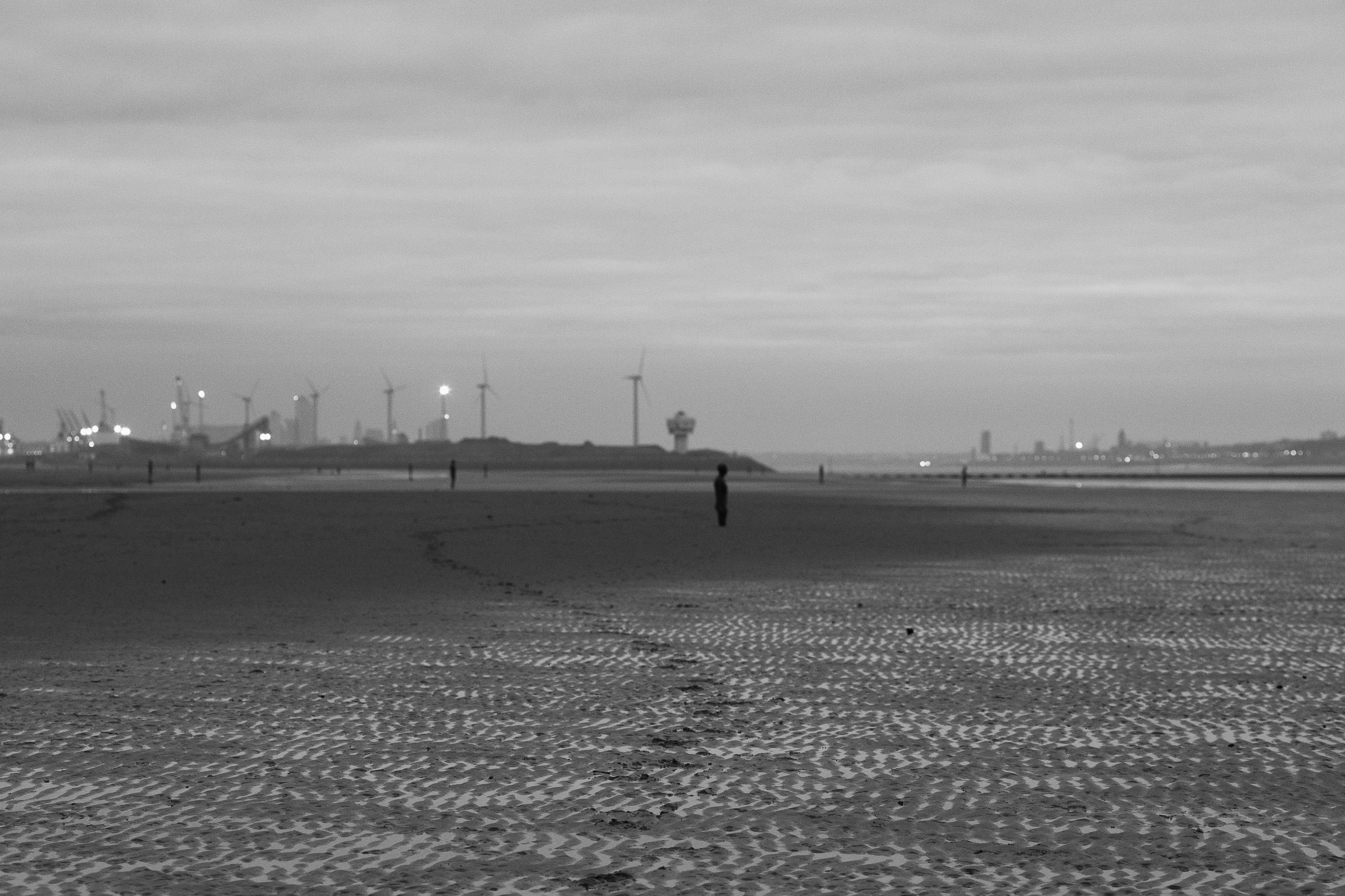 Antony Gormley's "Another Place" Statues on Crosby Beach. Footsteps seen in the sand. The Port of Liverpool Wind Farm from Conrad energy in the distance.