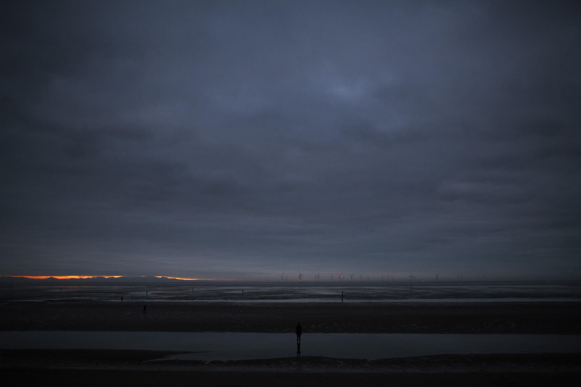 Antony Gormley's Another Place Statues on Crosby Beach at Twilight, with the Burbo Bank Offshore Wind Farm in the distance.