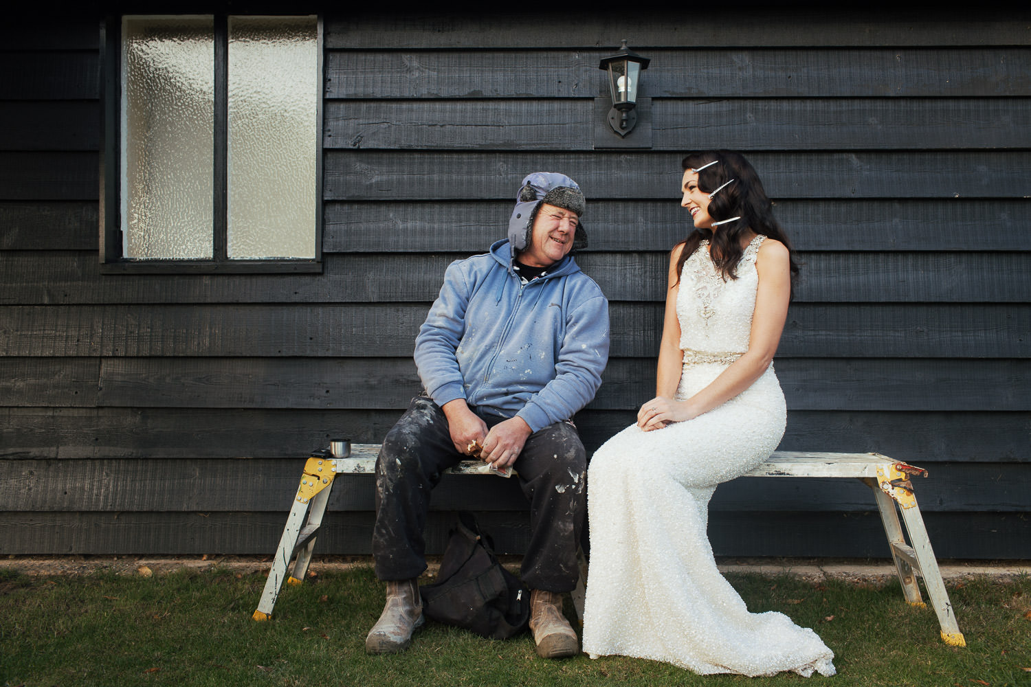 At the wedding venue, High House, near South Woodham, Amelia, manager of the bridal shop Bellissima, in a wedding dress, sits on a workbench with a handyman on his break.