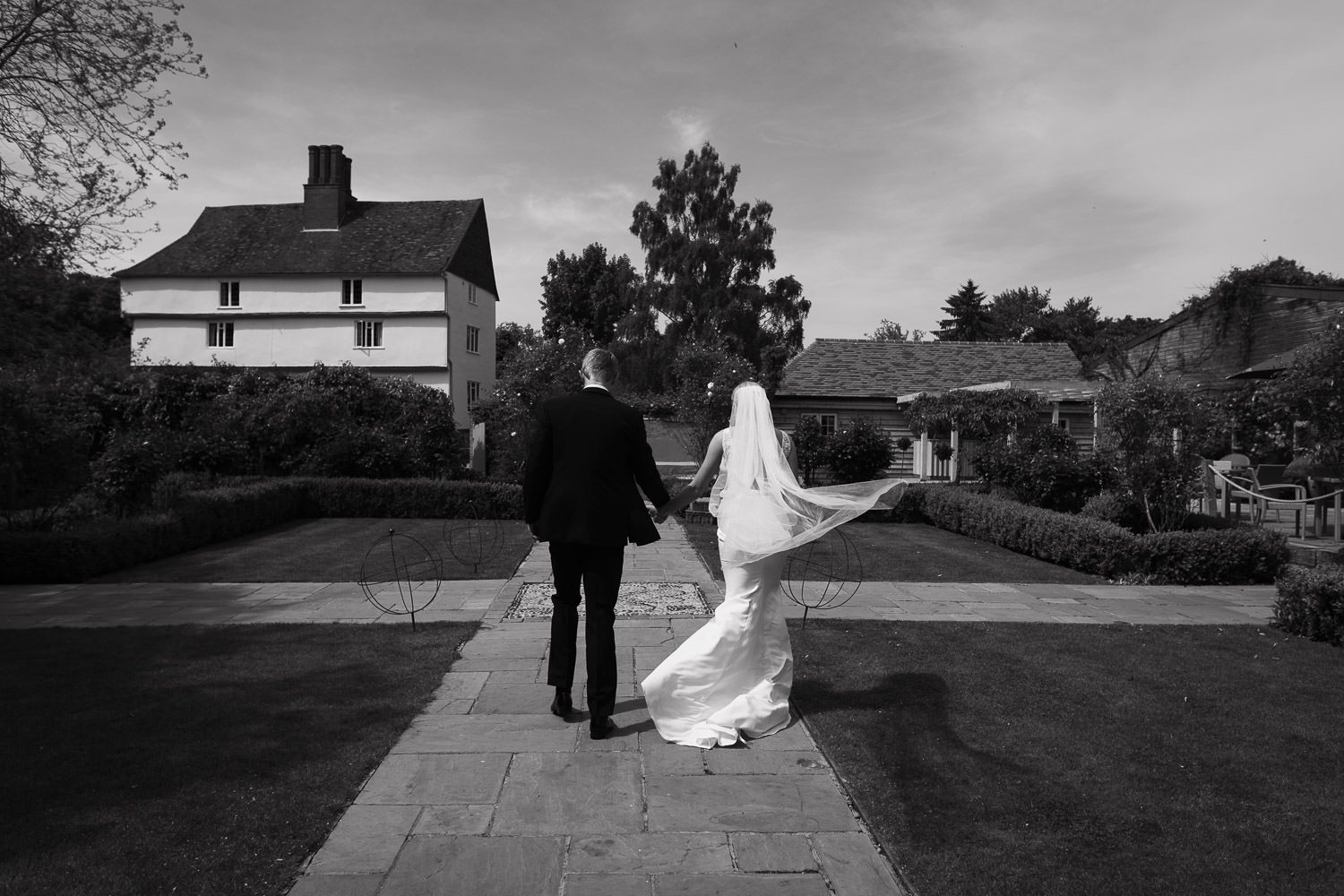 Best documentary wedding photography at Houchins venue. A photograph of a couple immediately after their outdoor wedding ceremony on a sunny day with blue skies. The bride wears the 'Jack' dress by Made With Love, from Halo & Wren. The groom is in a suit from The Grooms Room. Location: Houchins, CO6 1RT.