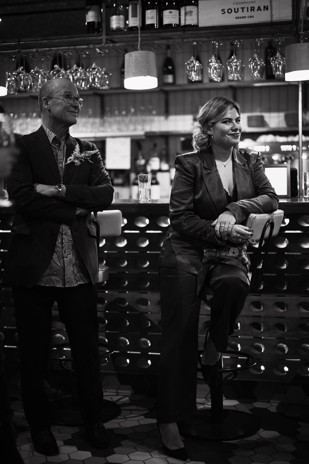 Woman in a satin suit leaning on a bar stool in the Humble Grape near Fleet St. She is smiling at the camera. Documentary London Wedding Photography by Essex photographer.