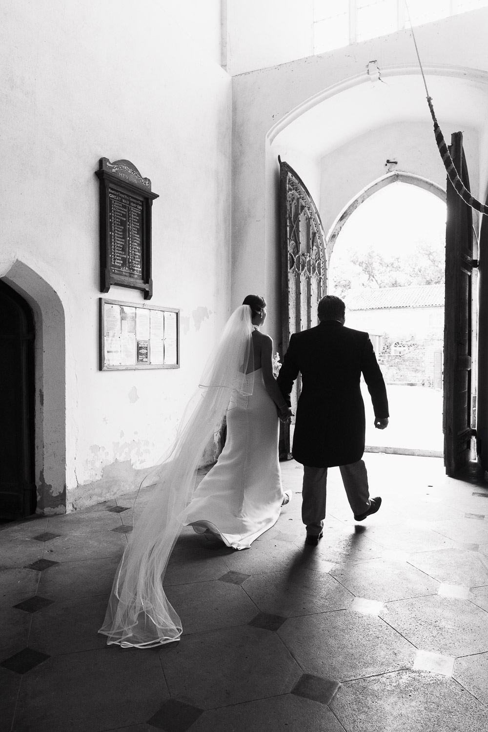 Church of St Peter & St Paul in Heydon: A Norfolk wedding. The bride and groom holding hands exiting the church after ceremony. Bride wearing bespoke dress from Katrine Mogensen. Flowers by Brunstead Blooms.