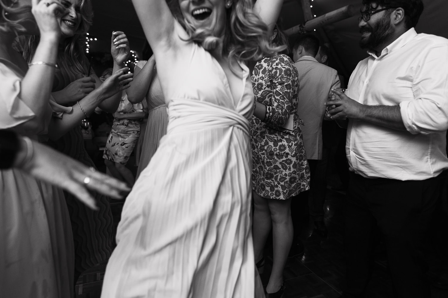 Bridesmaid jumps for joy while dancing at an evening reception in a tipi in a Suffolk garden, captured by a documentary wedding photographer from Essex.