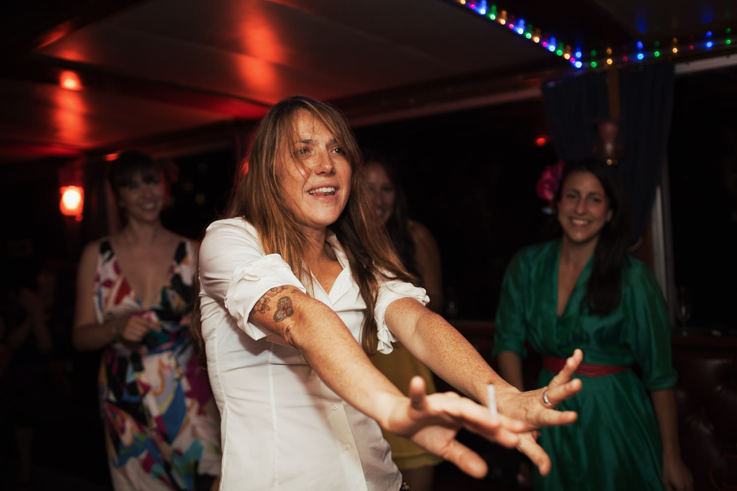 Black and white candid photograph of a woman dancing at a wedding, she's holding a cigarette.