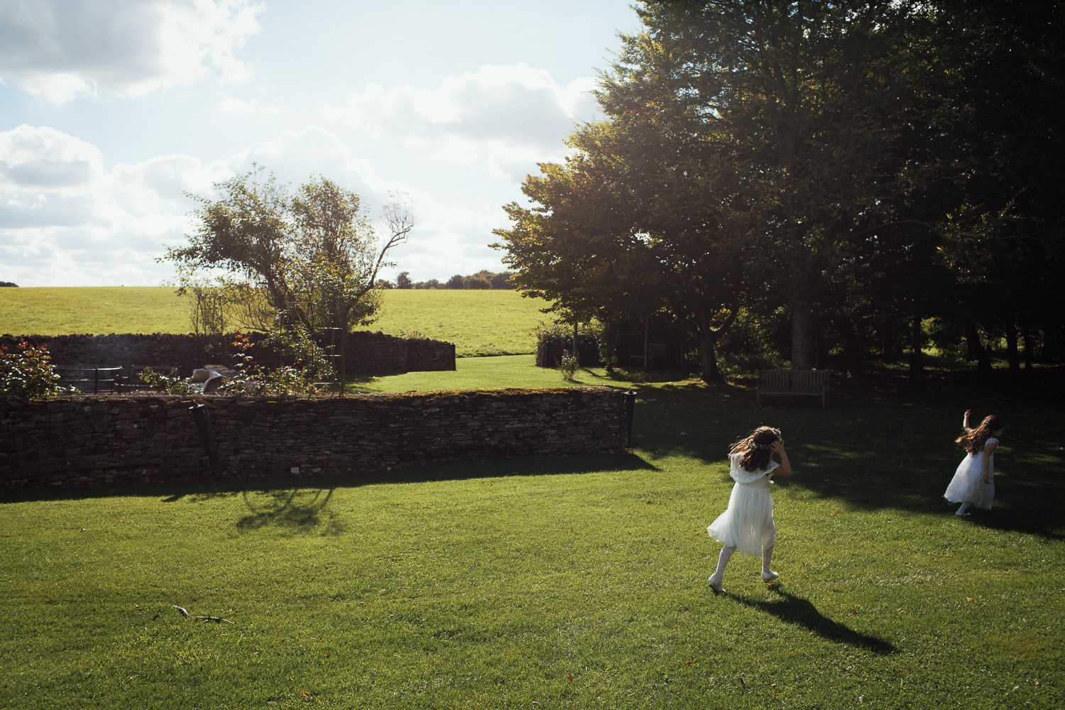 Two flower girls running on the lawn in the sunshine at Cripps Barn wedding venue. GL7 5BA