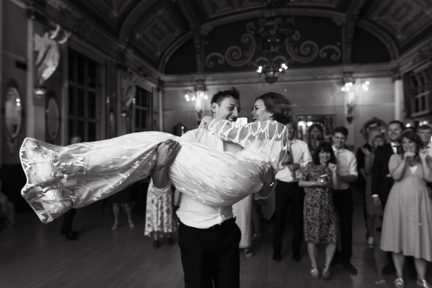 Groom picks up his wife and spins her around at a wedding reception at the Old Finsbury Town Hall. The bride, wearing the Willow dress from Halfpenny London. Captured in a documentary wedding photography style.