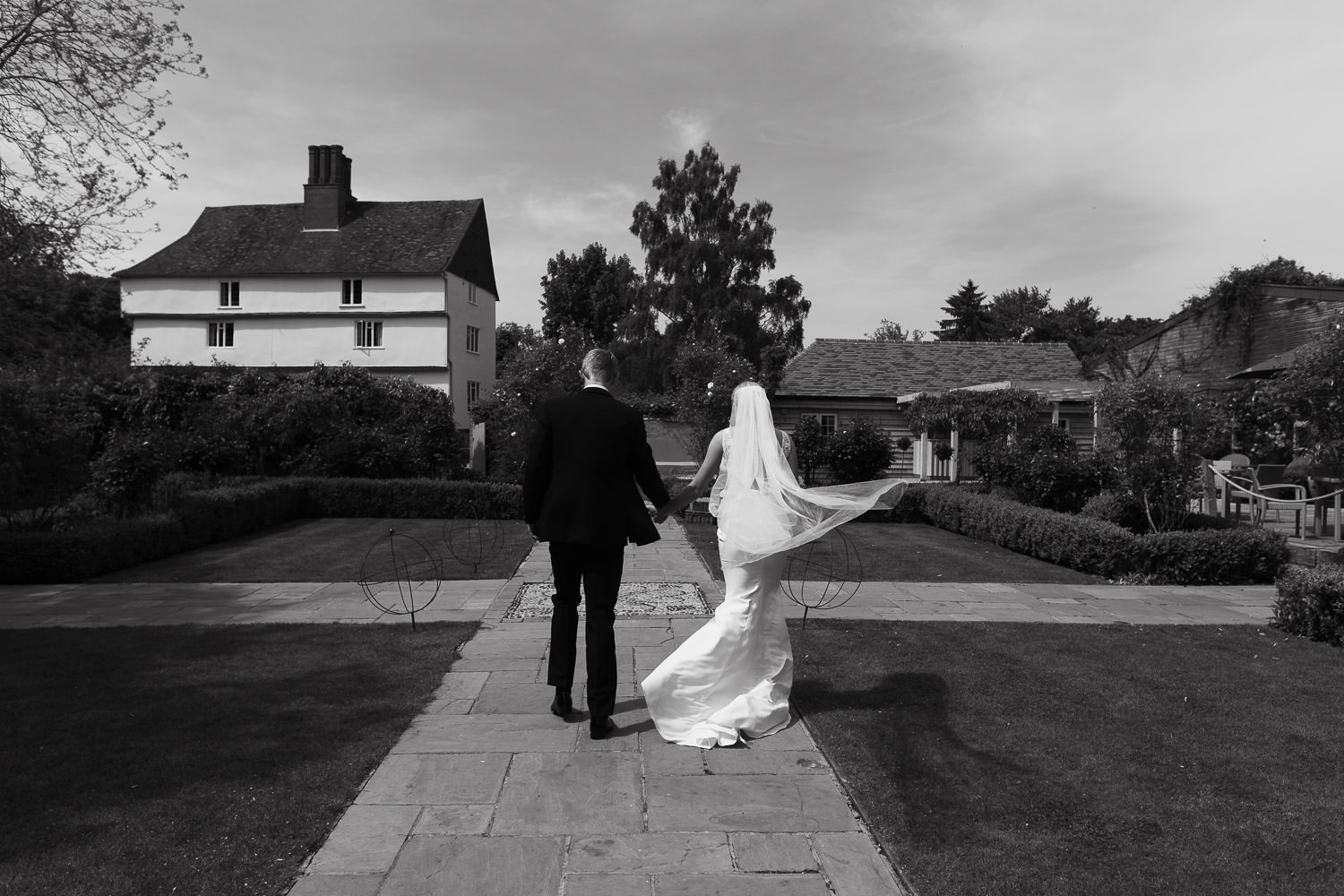 Best documentary wedding photography at Houchins venue. A photograph of a couple immediately after their outdoor wedding ceremony on a sunny day with blue skies. The bride wears the 'Jack' dress by Made With Love, from Halo & Wren. The groom is in a suit from The Grooms Room. Location: Houchins, CO6 1RT.