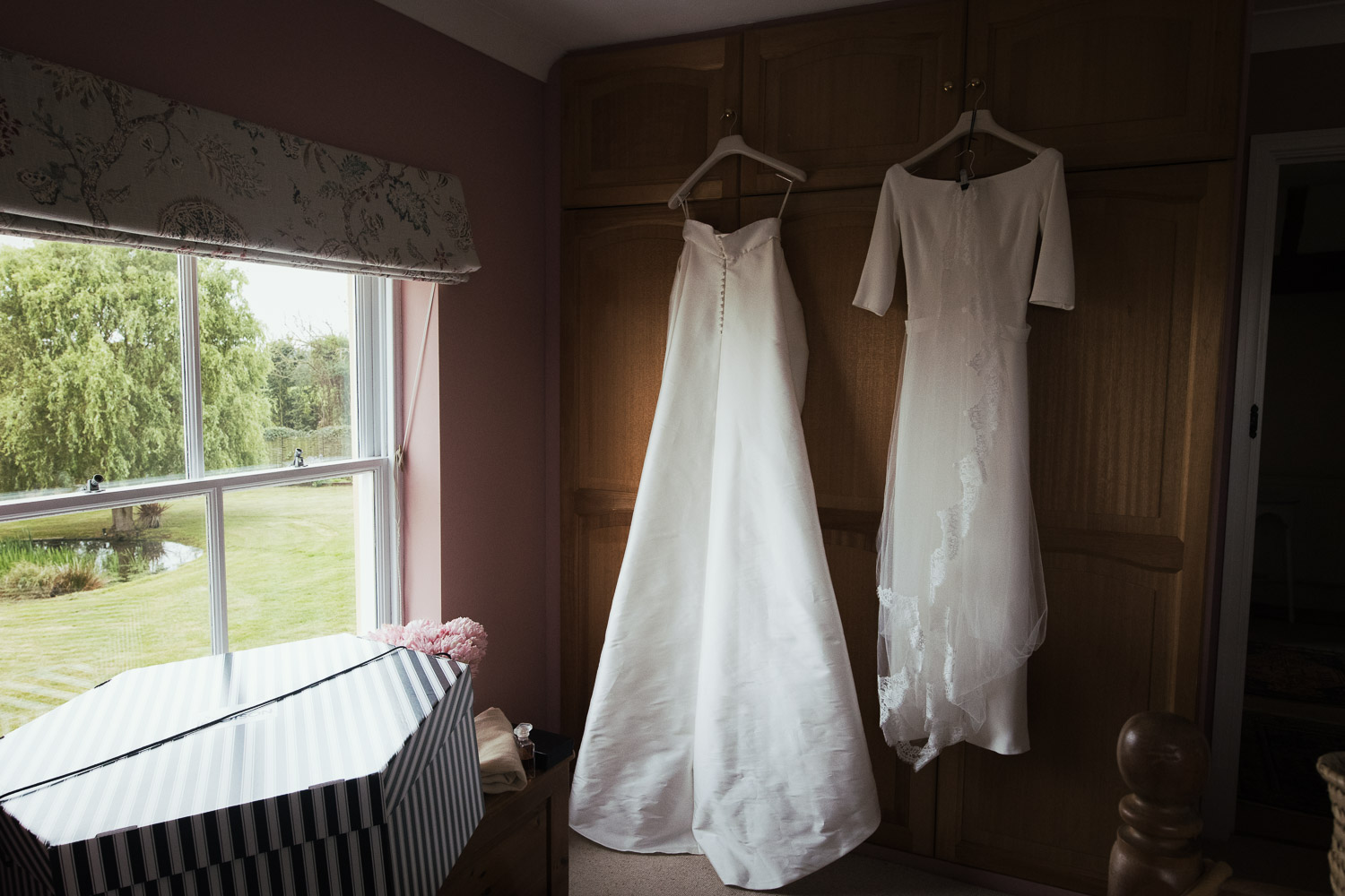 A dress and detachable overskirt from Miss Bush hangs on a wardrobe in a bedroom. Outside the window you can see trees.