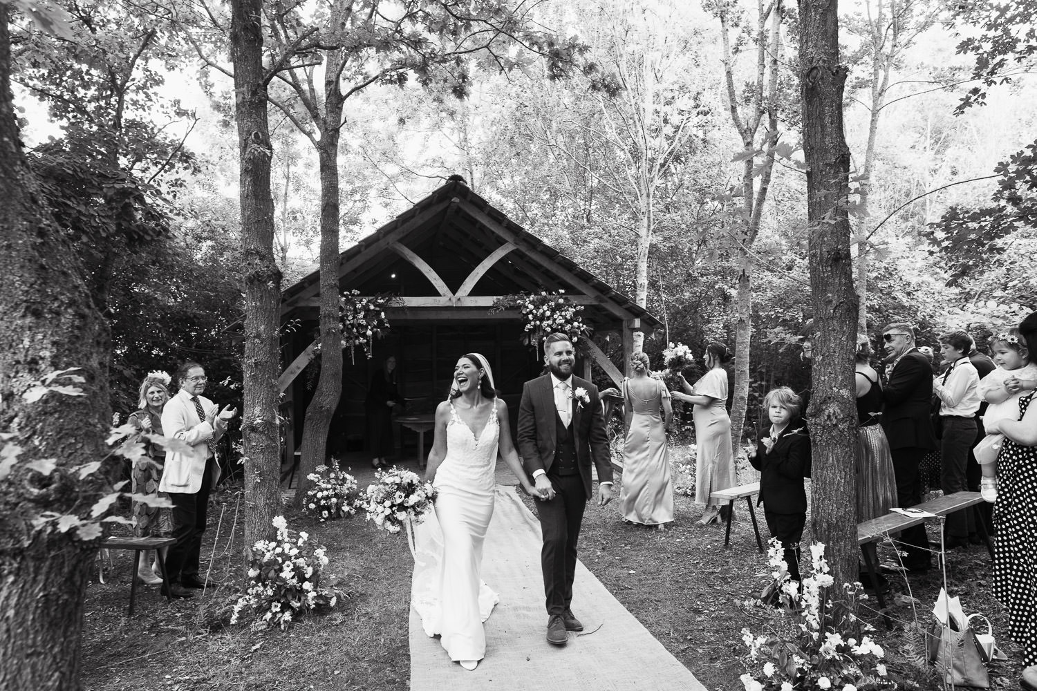 Newly married couple walking down the woodland ceremony glade aisle. Wearing Maggie Sottero style 22MW548B01