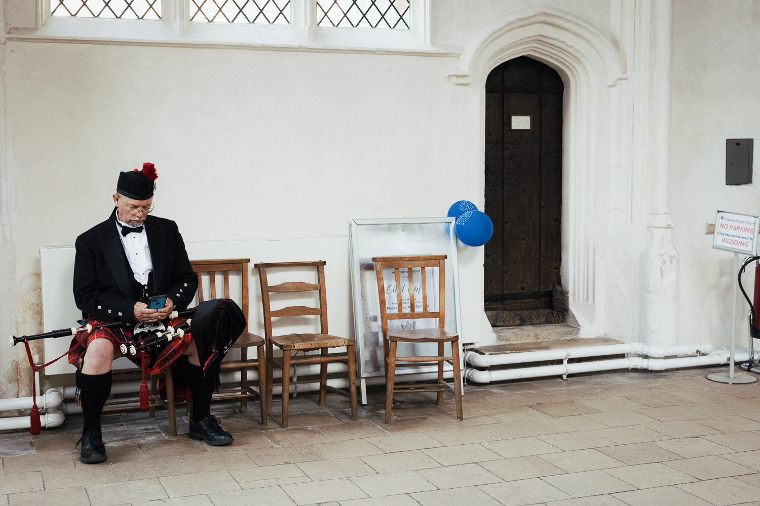 A bagpipe player waits sitting on a chair during an Essex church wedding in Thaxted.