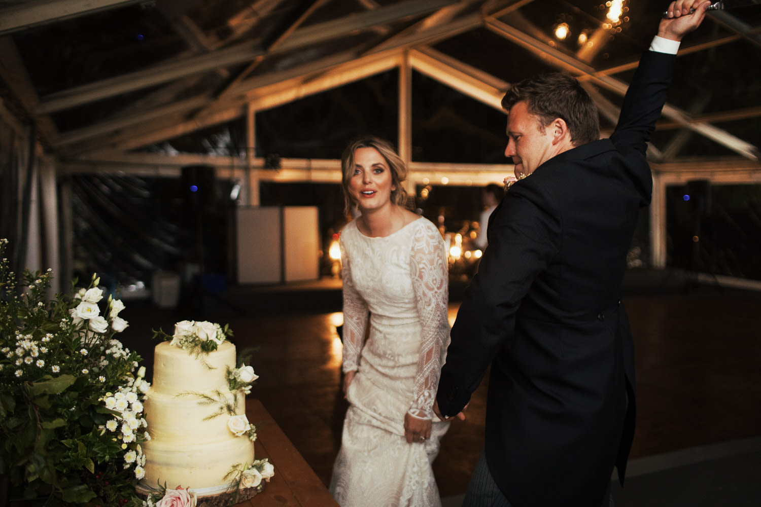 A woman hitches up her wedding dress as her new husband wields the knife to dramatically cut the cake. A marquee Essex wedding near South Woodham Ferrers.