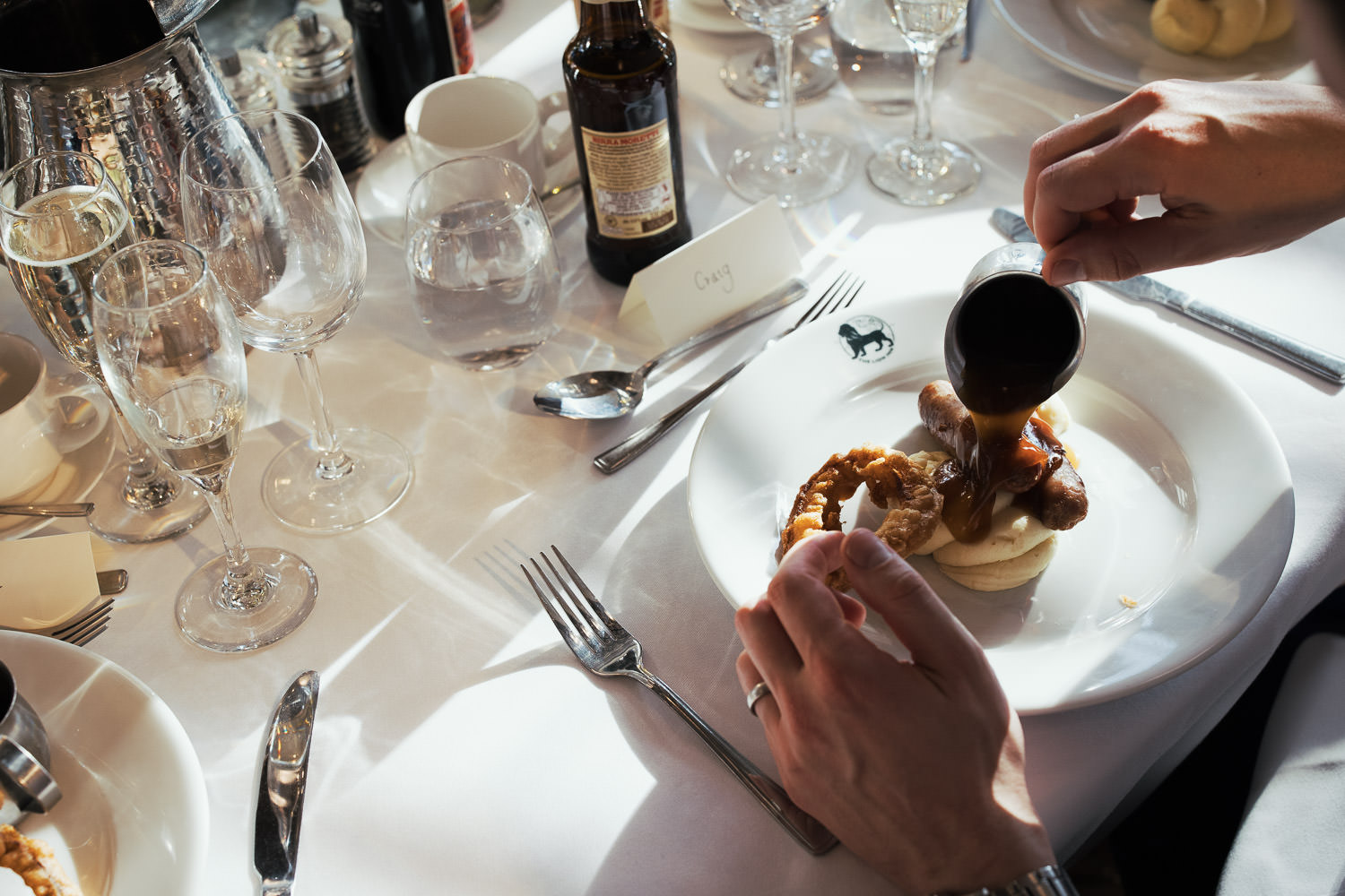 The Lion House Wedding Breakfast:
Cumberland Sausages Roast pork gravy, a beer-battered onion ring, and creamy mash. Served with vegetables.
Man pouring gravy on meal.