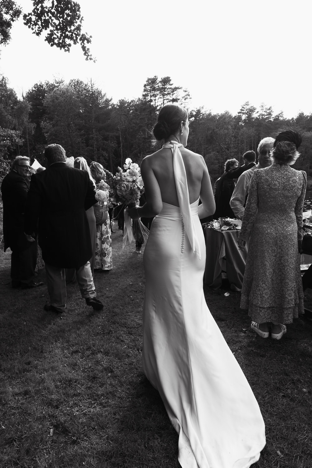 Bride walking by the lake at her Cawston wedding reception, surrounded by cheering guests. She wears a dress by Norfolk bridal designer, Katrine Mogensen.