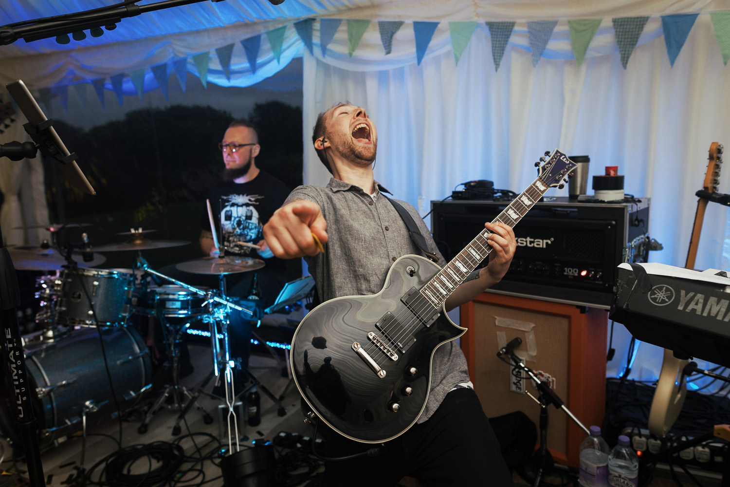 Al Bert Johnson of Monstaball plays his Black ESP LTD guitar and points at the camera, during a wedding reception in Shrewsbury. Blue bunting decorates the Muddy Boots Marquee.