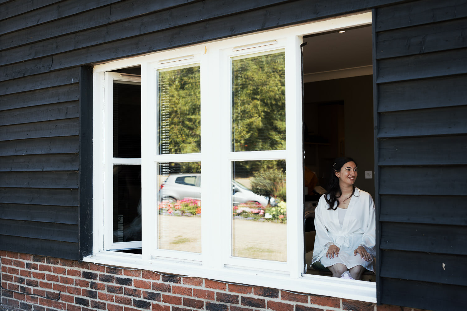 Looking through the window of the Little Bury Barn airbnb in Bury St Edmunds. A bride in a dressing gown is sat waiting for her wedding makeup.