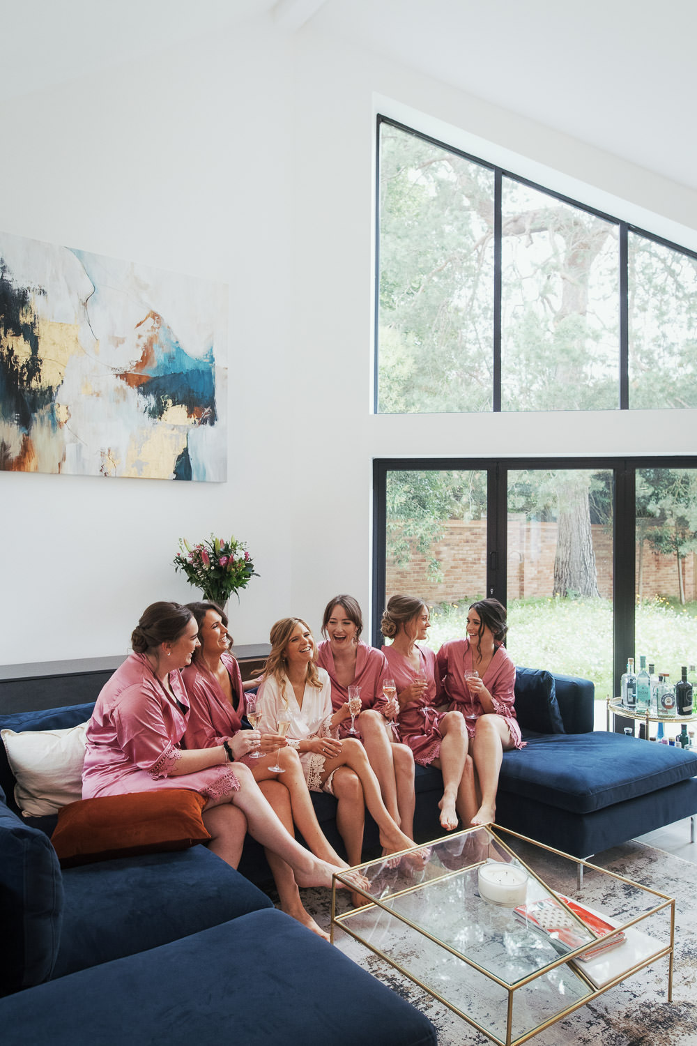 Bridal party sat on a sofa in a living area with a high ceiling and glass. A modern new home in Shiplake.