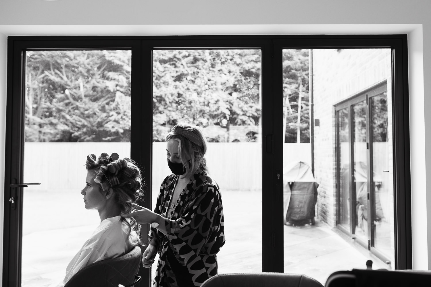 MUA hairdresser with the bride in her dress. Stood by glass patio doors.