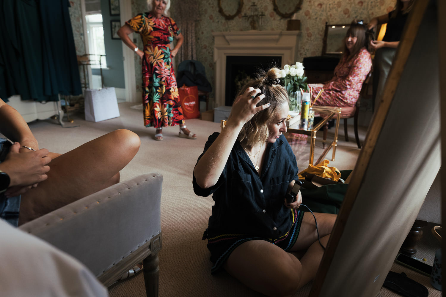 Prep in the bridal suite with Morris & Co. Mary Isobel Wallpaper on the wall. Woman using straighteners on hair. Baddow Park House.