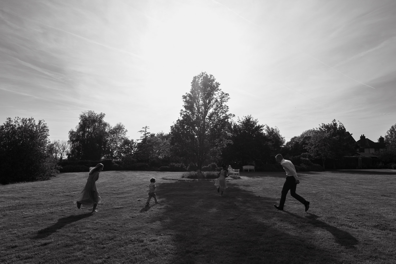 In the grounds of High House venue in Essex, children and teenagers play, running around in the sunshine. Trees in background.