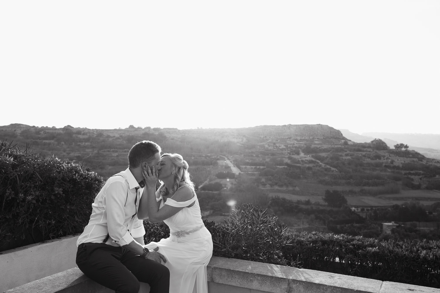 Bride and groom kiss while sitting on the wall at the Cornucopia Hotel in Gozo just after getting married.