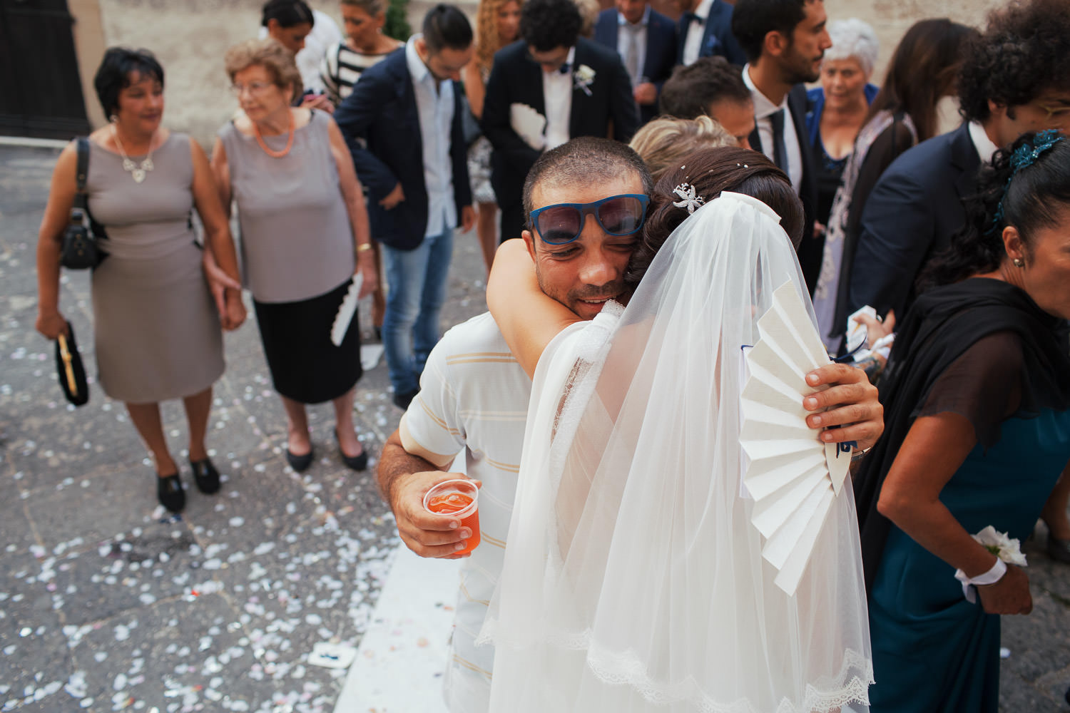 A man holding a fan and an aperol spritz hugs the bride.