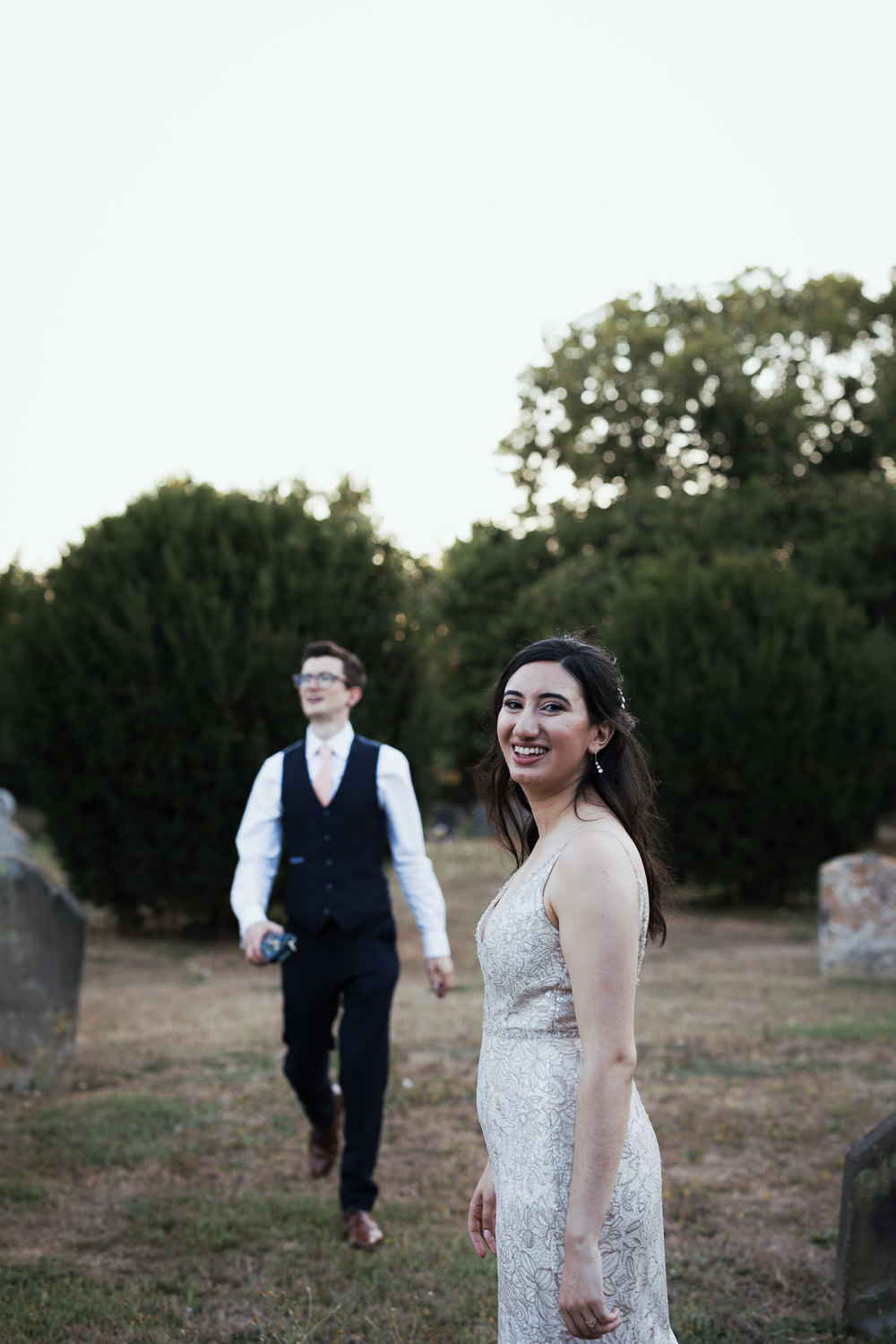 Bride and groom outside in the early evening at Alpheton Hall Barns. Bride is wearing a dress from The Bride St. Albans. She looks at the camera and smiles.