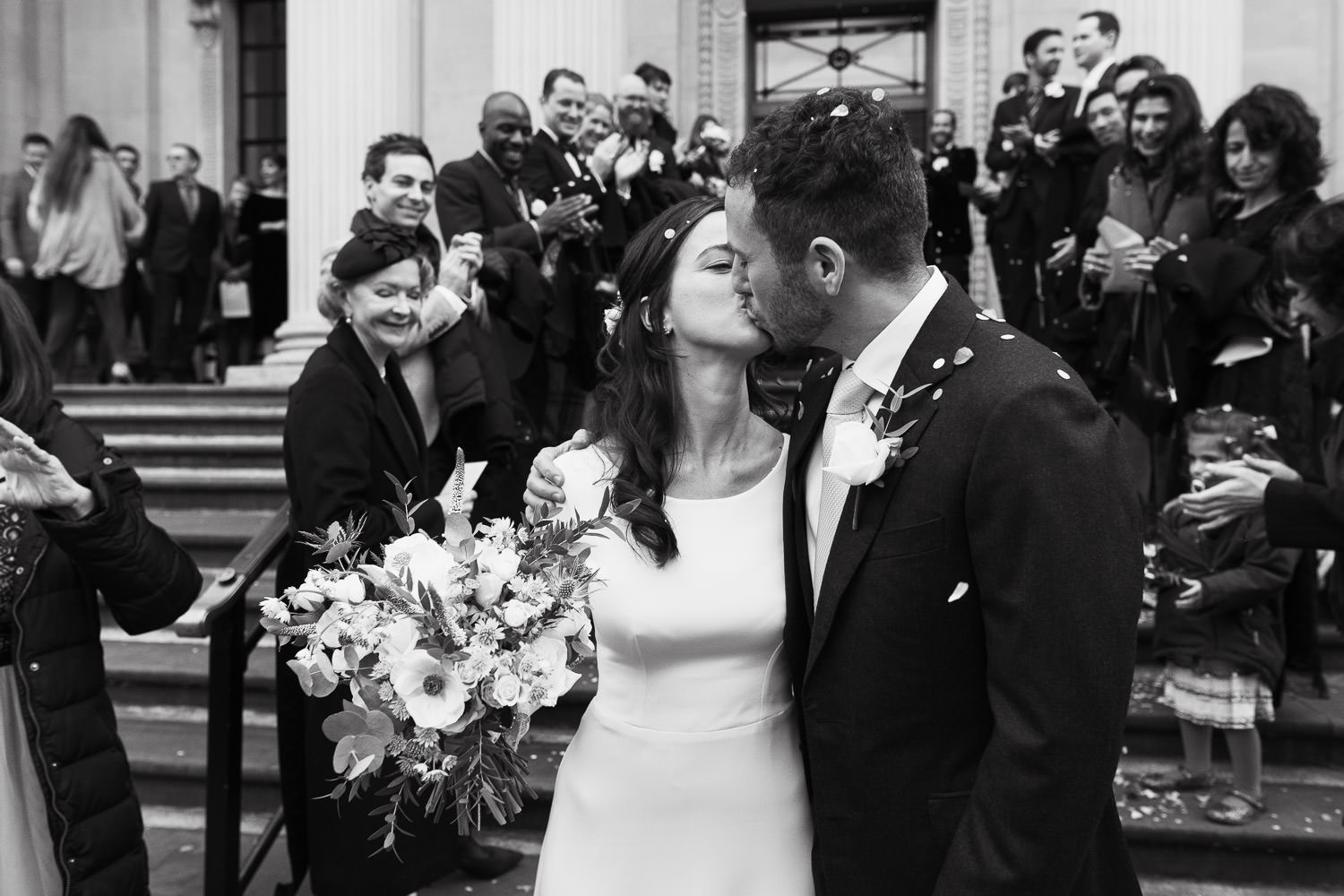 After getting married at the Old Marylebone Town Hall a couple walk down the steps. The wedding guests throw confetti at them.