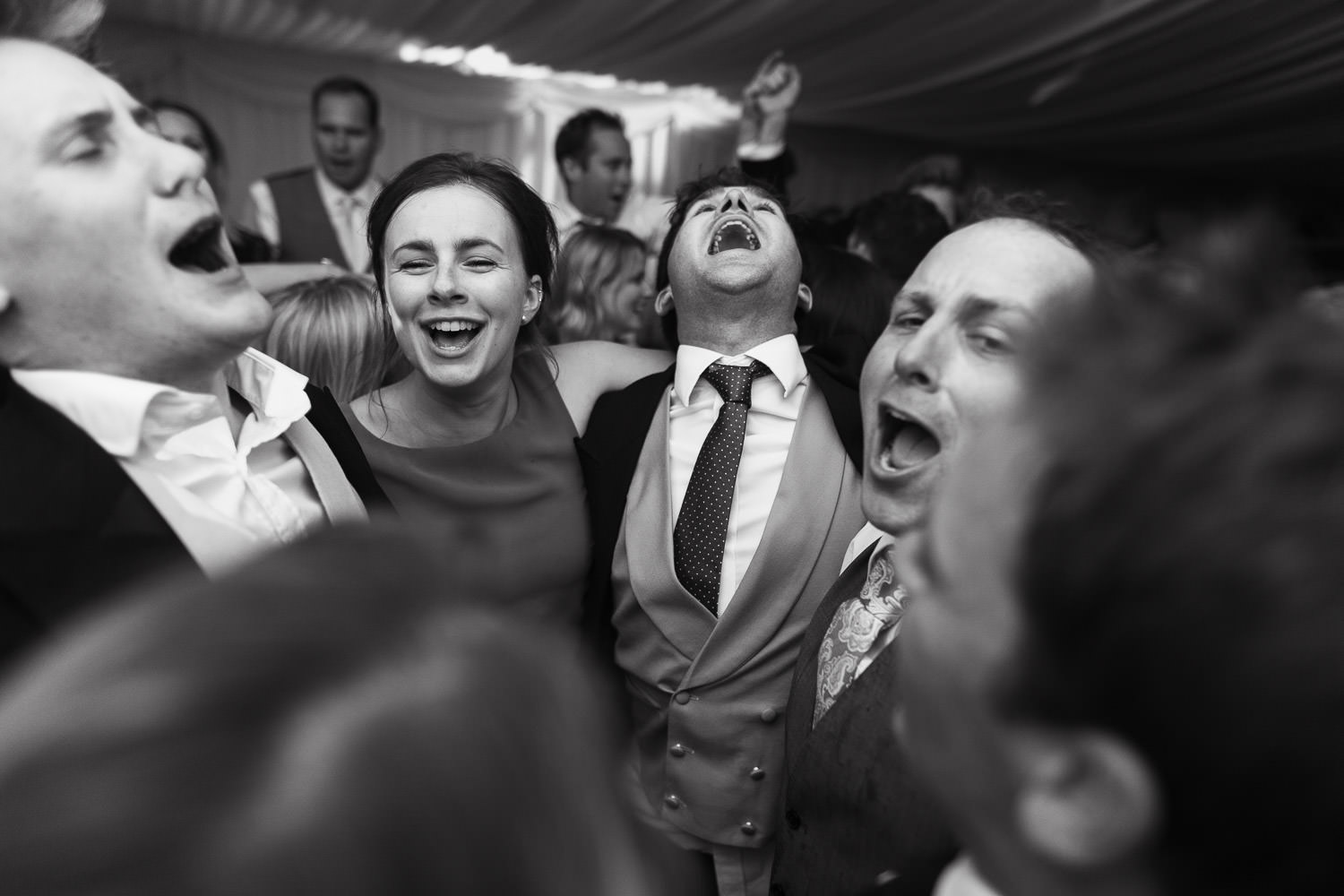 A group of friends huddled in a circle, singing loudly at the evening reception. Bridesmaid wearing Hobbs London Marielle Popover Dress.