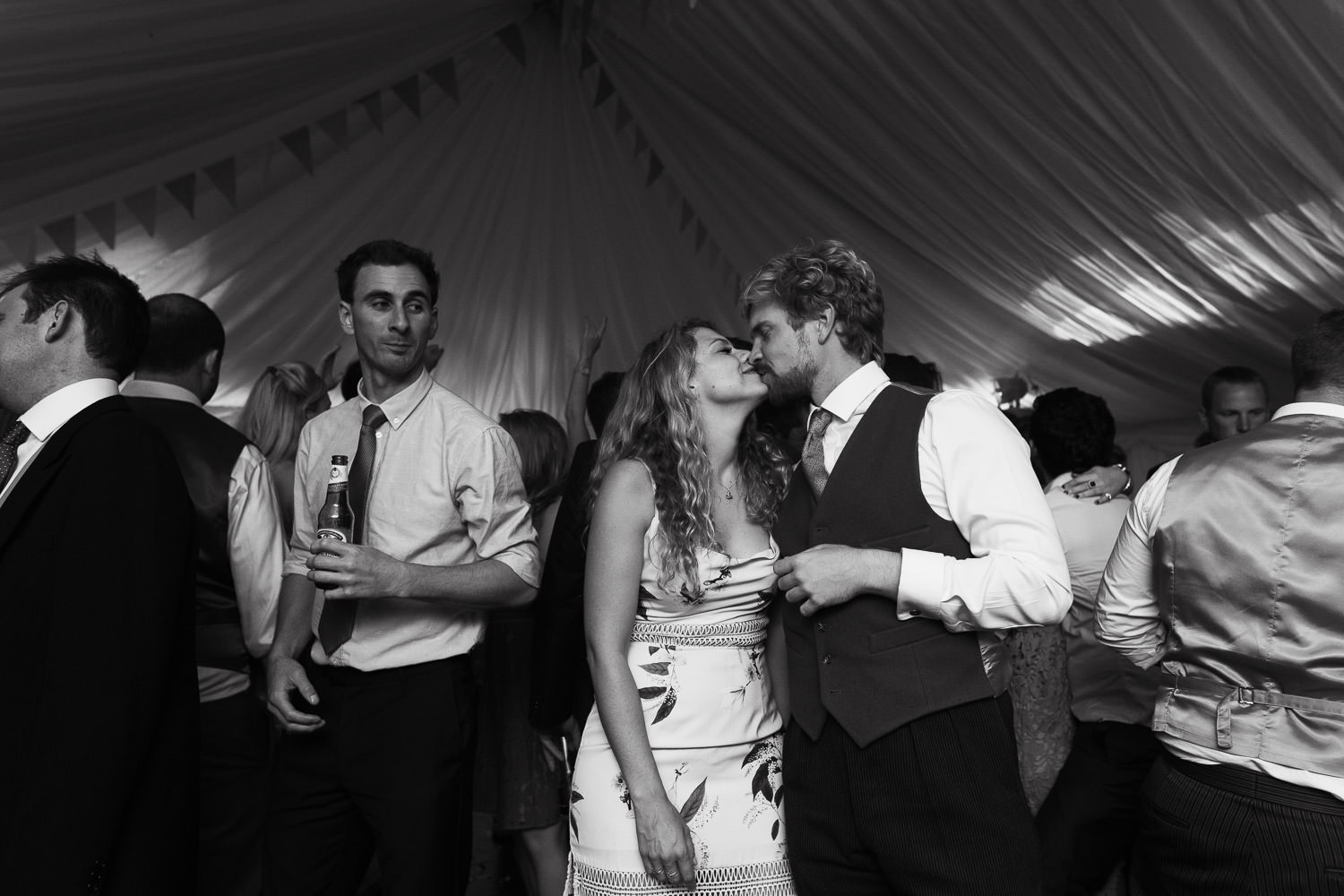 Woman in Keepsake The Label Floral Print Pencil Midi Dress kisses her fiancé on wedding dancefloor in marquee.