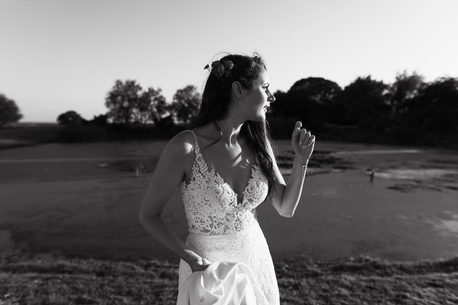 Bride with elegant bridal makeup by Kate Hughes, standing by a pond during an Essex wedding near South Woodham Ferrers. She wears a Stella York 6648 lace wedding dress from The Wedding Shop in Colchester. Unposed documentary wedding photography by Tracy Morter.