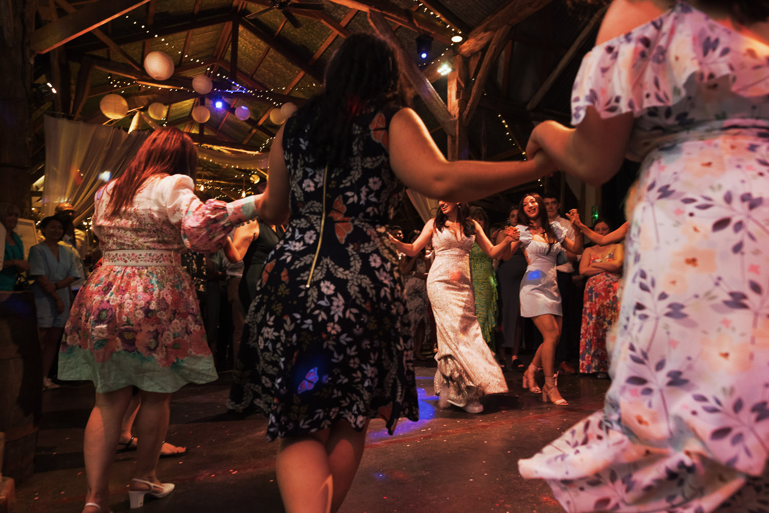 Black and white wedding reception photography at Alpheton. Women join hands and dance in a circle while bouzouki music plays.