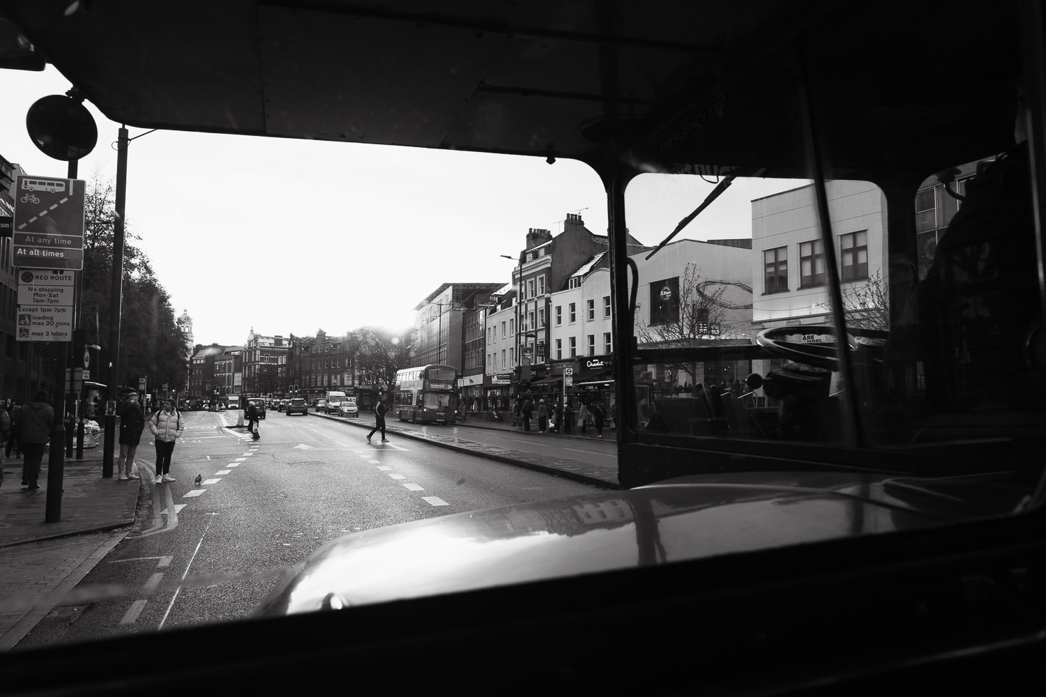 View from bus window as it travels down Upper St in Islington. The A1. You can see people crossing the road, a pigeon, Hotel Chocolat and Be at One.