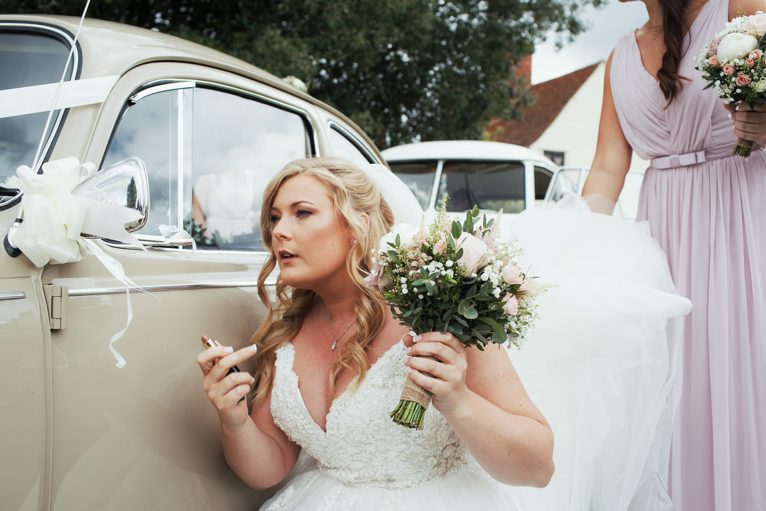 Bride checking her lipstick in the wing mirror of a beige 1968 Volkswagen Beetle.