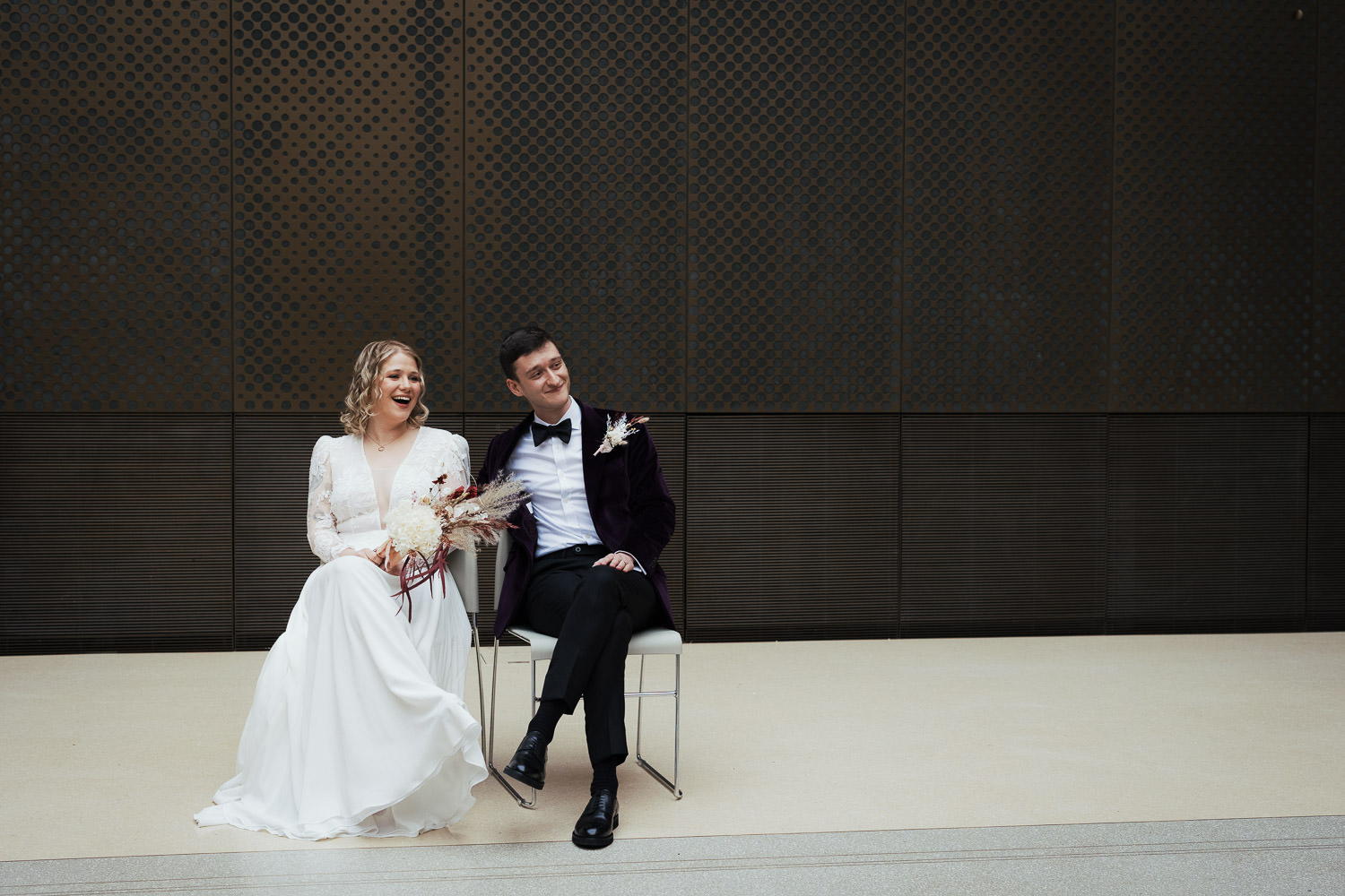 Bride and groom seated and smiling during their wedding ceremony in the North Atria of Hackney Town Hall, also the venue for Charli XCX's wedding.